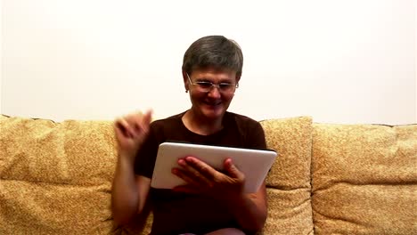 Eine-attraktive-erwachsene-Frau-ist-Video-Chat-mit-ihrer-Familie,-auf-einem-Tablet-PC,-sitzen-auf-einem-Sofa-zu-Hause.