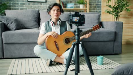 Creative-teenager-recording-video-about-guitar-holding-instrument-talking