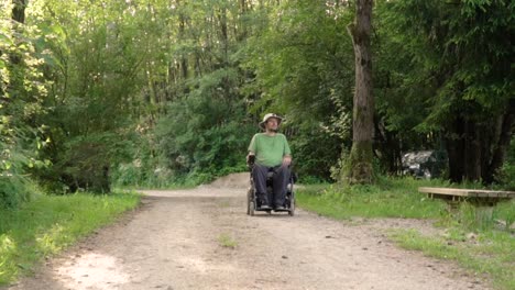 Slowmotion-portrait-of-disabled-young-man-in-a-wheelchair-observing-nature-around-him,-stopping-infront-of-the-camera