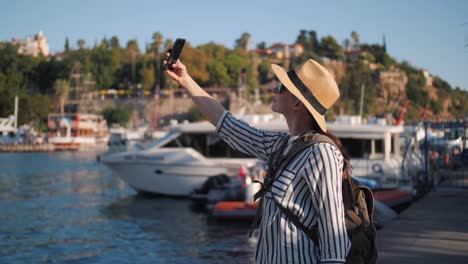 Millennial-hipster-mujer-turista-en-traje-casual-con-mochila-haciendo-selfie-en-muelle-de-yates,-puerto-deportivo