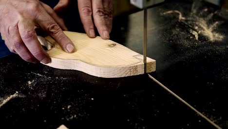 Close-up-footage-of-male's-hands-working-with-an-electric-cutting-machine.-High-angle-footage-of-a-man-cutting-a-fish-shape-wooden-pattern-on-a-table.-Slow-motion