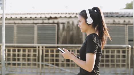 Hermosa-atleta-femenina-corriendo-usando-auriculares-usando-un-teléfono-inteligente-escuchando-música-mientras-camina-en-la-ciudad-urbana.-Jogging-estilo-de-vida-saludable.