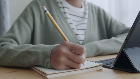 Mano-de-mujer-asiática-haciendo-la-tarea-y-aprendiendo-en-línea-a-través-de-la-comunicación-por-Internet-en-la-tableta-en-casa