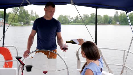 mujer-vierte-vino-de-la-botella,-descansar-en-el-agua,-familia-pareja-bebiendo-vino-en-barco,-pareja-romántica-bebe-bebida-roja