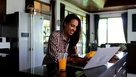 Chica-uso-portátil-en-cocina-chateando-en-línea-joven-estudio-casa-moderna-Interior