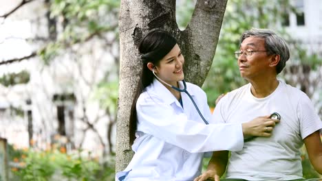 Young-female-doctor-using-the-stethoscope-listen-to-elderly-patient-heartbeat-in-hospital-garden