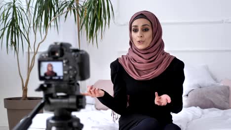 Young-beautiful-indian-girl-in-hijab-blogger-talking-on-camera,-counts,-outraged,-gesturing,-white-room,-home-comfort-in-background.-Close-up-50-fps