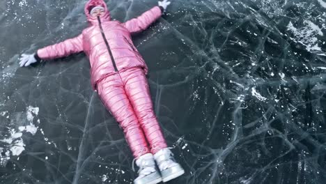 Mädchen-fliegt-und-rollt-auf-dem-Eis.-Junges-Paar-hat-Spaß-beim-Winterspaziergang-Hintergrund-von-Eis-der-zugefrorenen-See.-Liebhaber-Lüge-auf-klares-Eis-mit-Rissen,-haben-Sie-Spaß,-küssen-und-umarmen.-Ansicht-von-oben.