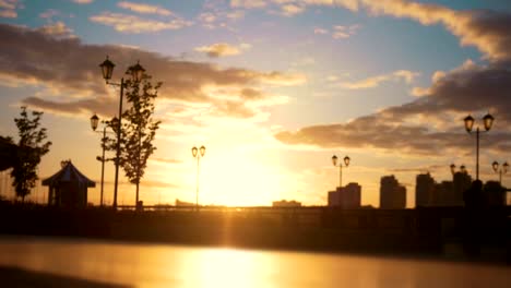 Caring-man-with-a-disabled-woman-in-wheelchair-walking-through-the-quay-at-sunset