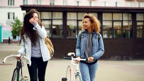 Dolly-Schuss-von-attraktiven-Girls-Freunde-zu-Fuß-mit-dem-Fahrrad-entlang-der-Straße-mit-schönen-alten-Gebäuden-und-gerne-reden.-Aktiven-Lifestyle-und-Tourismus-Konzept.