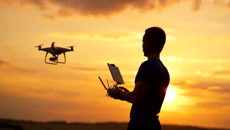 Der-Mann-kontrolliert-Quadrocopter-auf-dem-Sonnenuntergang-Hintergrund