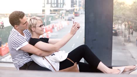 Pareja-romántica-multiétnico-feliz-sentado-en-un-puente-de-la-calle-de-Nueva-York,-tomando-selfie-smartphone-y-divertirse-sonriendo