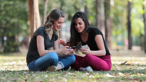 Amigas-mirando-sus-celulares-compartir-chismes-de-los-medios-sociales-al-aire-libre