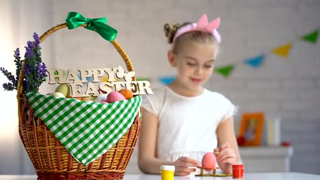 De-vacaciones-feliz-signo-de-Pascua-en-cesta,-huevos-de-pintura-linda-chica-sentada-en-la-mesa,