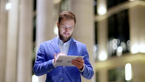 Medium-waist-up-shot-of-middle-aged-businessman-smiling-while-text-messaging-on-tablet-computer-and-thinking-of-reply