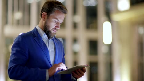 Side-view-medium-shot-of-middle-aged-businessman-in-suit-using-application-on-tablet-computer-outdoors-in-evening