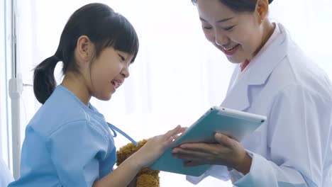 Female-doctor-showing-digital-tablet-computer-and-talking-with-young-patient-girl-with-happy-emotion.