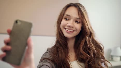 Young-woman-taking-selfie-photo-on-mobile-phone-in-bedroom