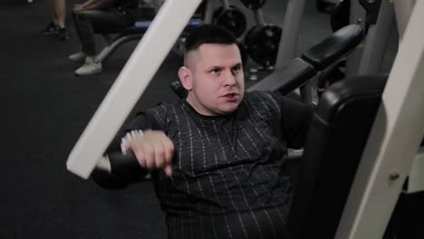 Cheerful-fat-man-performs-a-wrong-exercise-in-the-gym.-For-the-first-time-in-a-fitness-club