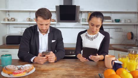 Man-and-woman-sit-in-their-kitchen-in-the-morning