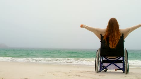 Seitenansicht-der-jungen-kaukasischen-Frau,-die-mit-Armen-sitzt,-die-auf-dem-Rollstuhl-am-Strand-4kouple-hav-ausgestreckt-sind.