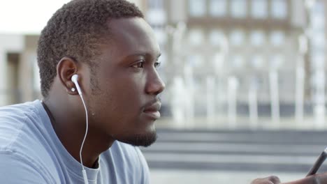 Hombre-africano-feliz-escuchando-música-en-el-teléfono-inteligente-y-sonriendo-a-la-cámara