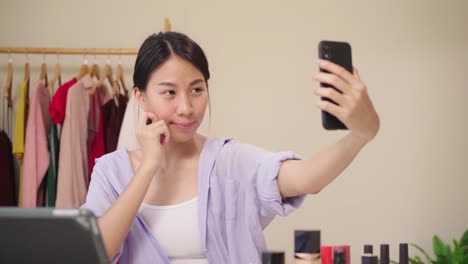 Feliz-hermosa-joven-asiática-utilizando-smartphone-selfie-streaming-en-vivo-en-línea-a-la-red-social.-Belleza-blogger-presenta-cosméticos-de-belleza-sentados-en-la-cámara-frontal-de-la-tableta-para-la-grabación-de-vídeo.