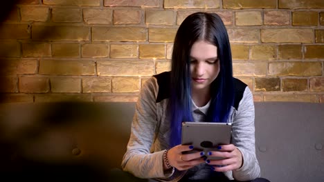 Closeup-shoot-of-young-pretty-caucasian-female-typing-on-the-tablet-while-sitting-on-the-couch-in-a-cozy-apartment-indoors