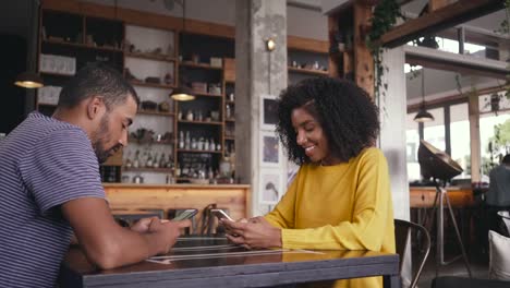 Young-couple-sitting-in-cafe-using-their-smart-phone