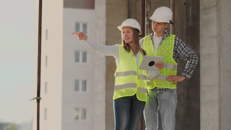 Trabajadorde-la-construcción-hombre-y-arquitecto-mujer-en-un-casco,-discutir-el-plan-de-construcción-de-la-casa,-hablarse-unos-a-otros-sobre-el-diseño,-sosteniendo-una-tableta,-mirar-los-dibujos,-fondo-de-los-rayos-del-sol