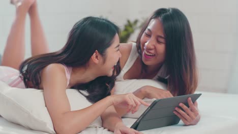 Asian-Lesbian-couple-using-tablet-after-wake-up,-watching-movie-lying-on-bed-in-bedroom.