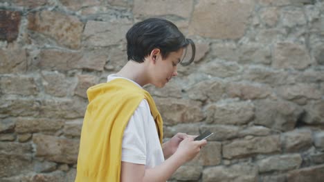 Slow-motion-of-cheerful-teenager-using-modern-smartphone-walking-outdoors