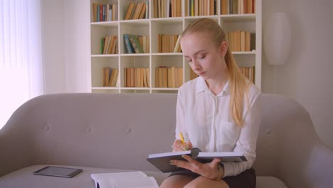 Nahaufnahme-Porträt-von-jungen-hübschen-kaukasischen-blonden-Frau-mit-dem-Tablet-und-Studium-sitzen-auf-der-Couch-in-der-Wohnung