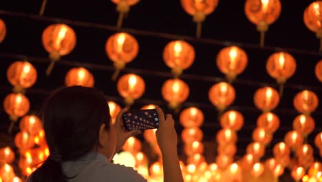 Asiatische-Frau-machen-ein-Foto-mit-dem-Smartphone.-Schöne-Laternen-im-Hintergrund.-Immer-noch-geschossen.