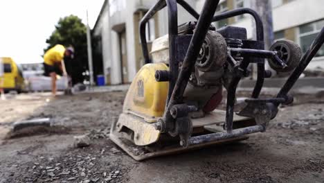 Vibrationspflastersteinmaschine-für-die-Veredelung-auf-einer-Gehwegbaustelle,-die-während-der-Straßenbauarbeiten-auf-einem-Boden-und-Steinen-bleibt.