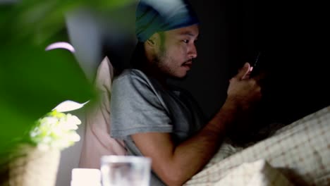 Attractive-Asian-man-using-a-mobile-phone-while-Lying-on-Bed-at-home.-Browsing-social-media-and-watching-a-video.