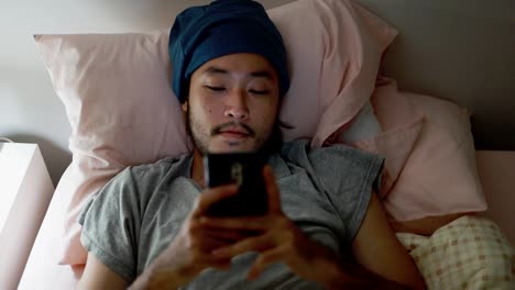 Cierra-a-un-hombre-asiático-guapo-usando-un-teléfono-móvil-mientras-estás-acostado-en-la-cama-en-casa-tarde-en-la-noche.-Navegar-por-las-redes-sociales-y-ver-un-video.