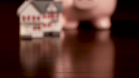 Pan-of-Piggy-Bank-y-Miniature-House-en-superficie-de-madera-oscura