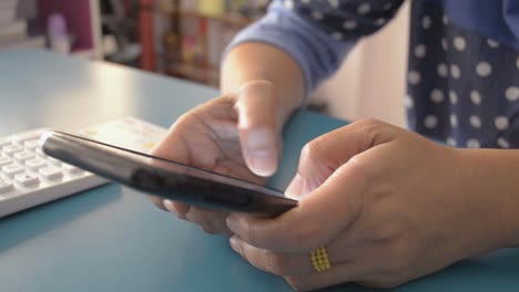 Mujer-usando-teléfono-inteligente-en-el-escritorio-en-casa.