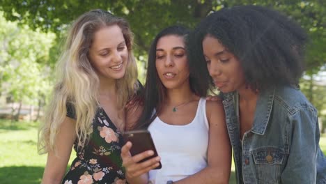 Feliz-diversas-amigas-jóvenes-están-viendo-contenido-en-la-pantalla-del-teléfono-inteligente-en-el-parque---amigos-en-el-parque-utilizando-una-aplicación-móvil