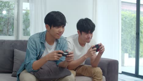 Young-Asian-gay-couple-play-games-at-home,-Teen-korean-LGBTQ-men-using-joystick-having-funny-happy-moment-together-on-sofa-in-living-room-at-house.