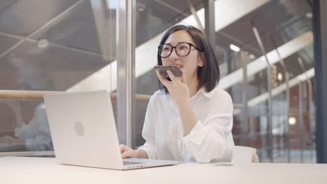 Asiática-empresaria-grabando-mensaje-de-voz-en-el-lugar-de-trabajo