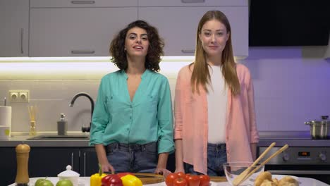 Mujeres-jóvenes-alegres-sonriendo-entre-sí,-de-pie-en-la-cocina,-pareja-lesbiana