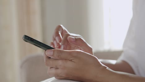 Vista-lateral.-Mano-de-mujer-joven-están-utilizando-el-teléfono-inteligente-mientras-se-sienta-en-el-sofá-en-la-sala-de-estar.