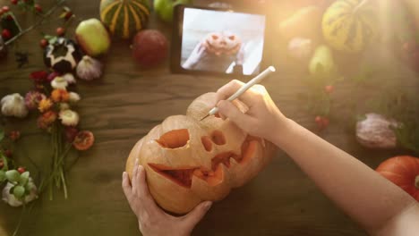 Female-carves-a-Halloween-decor-pumpkin-with-tablet-manual