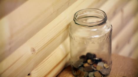 pennies-droped-into-a-transparent-jar-on-wooden-background