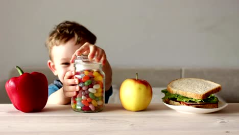 niedlicher-kleine-Junge-nimmt-Glas-mit-bunten-Süßigkeiten