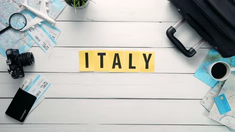 Top-view-time-lapse-hands-laying-on-white-desk-word-"ITALY"-decorated-with-travel-items