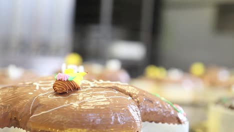 pastry-chef-hands-garnish-Easter-sweet-bread-cakes-with-flowers-fondants-sugar-paste,-closeup-on-the-worktop-in-confectionery