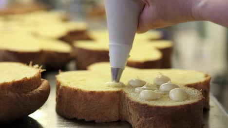 manos-de-chef-de-pastelería-rellenos-de-tortas-de-pan-dulce-de-Pascua-con-crema-pastelera,-closeup-en-la-encimera-en-confitería